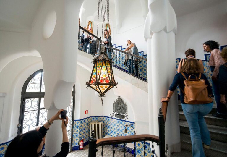 Visitors exploring the interior staircase of Torre Bellesguard with colorful ceramic tiles and a vibrant hanging lantern